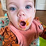 baby, blue_eyes, bib, baby_food, pink_bib, orange_food_stain, baby_seat, curious_expression, open_mouth, close_up, infant, child, clothing, indoor, face, person, cute, young_child, surprised, feeding_time