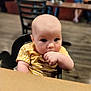 Adalynn joined the competition — help win amazing prizes! baby, child, high_chair, striped_shirt, yellow_clothing, indoor, restaurant, table, hand, face, sitting, curious, person, furniture, wood_floor, blurred_background, infant, young_child, casual_clothing, cute