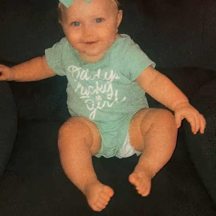 Kelsey is registered to the contest to win money with this photo: baby, child, infant, girl, sitting, couch, bow, hair_accessory, onesie, green_clothing, smiling, happy, portrait, indoor, furniture, barefoot, outstretched_arms, dark_background, social_media_screenshot, photography