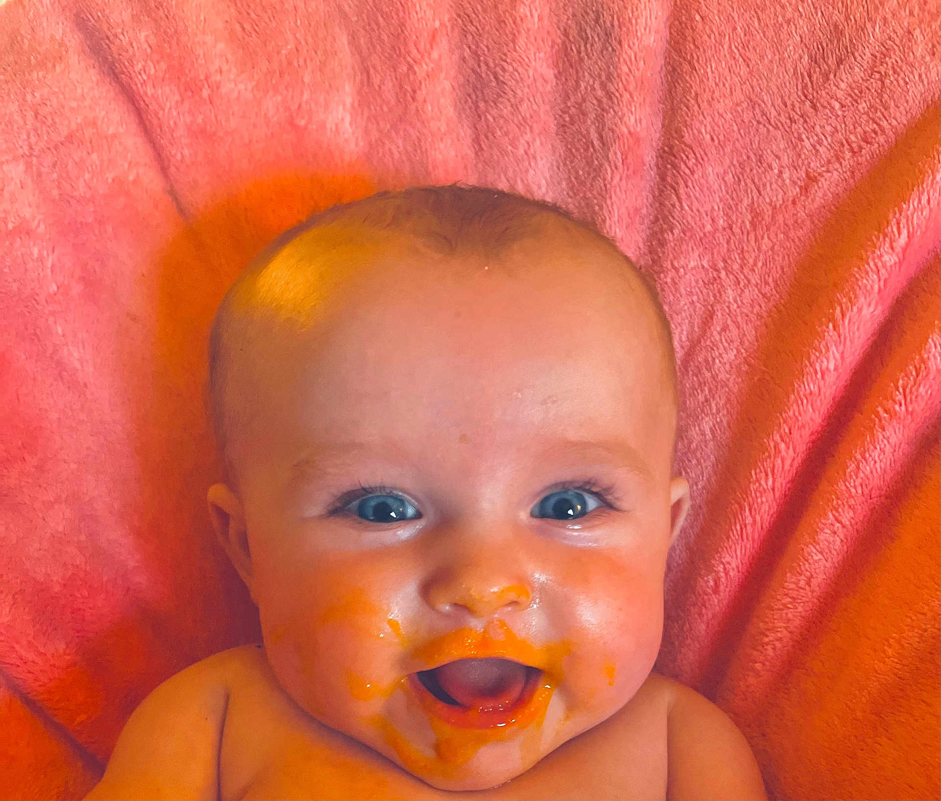Chloe Ann is registered to the contest to win money with this photo: baby, infant, face, blue_eyes, messy, food, orange_puree, smiling, happy, cheeks, mouth_open, skin, head, blanket, pink, cute, child, portrait, expression, closeup