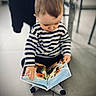 toddler, child, book, reading, striped_clothing, socks, floor, tile, indoor, person, concentration, storybook, dragon, colorful, cute, young_child, seated, playing, casual, home
