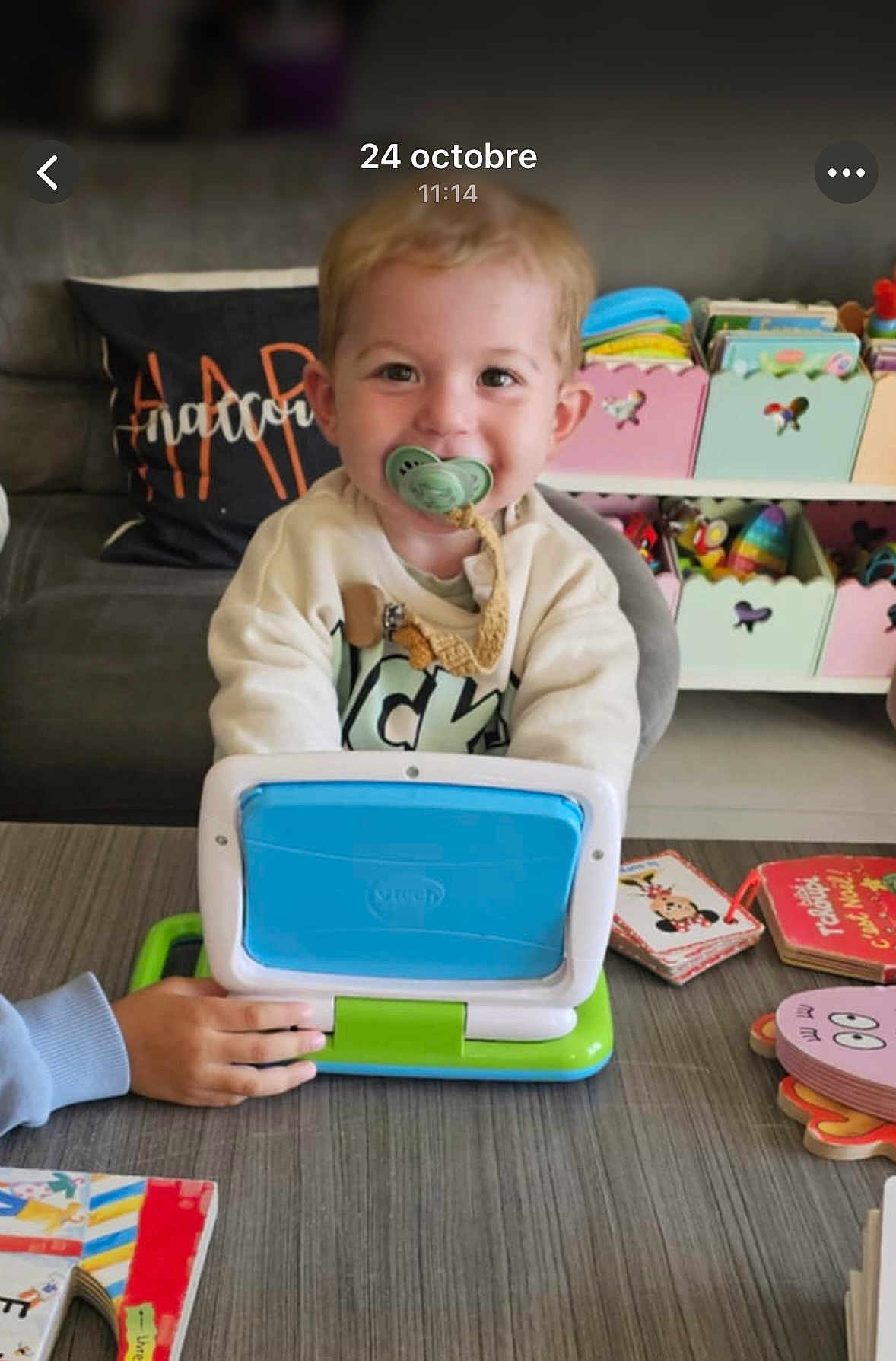 Dario a rejoint le concours — aidez-le/la à gagner de superbes lots ! toddler, child, pacifier, toy_laptop, table, books, toys, smile, indoor, living_room, couch, storage_boxes, colorful, happy, play, person, furniture, young_child, clothing, hand