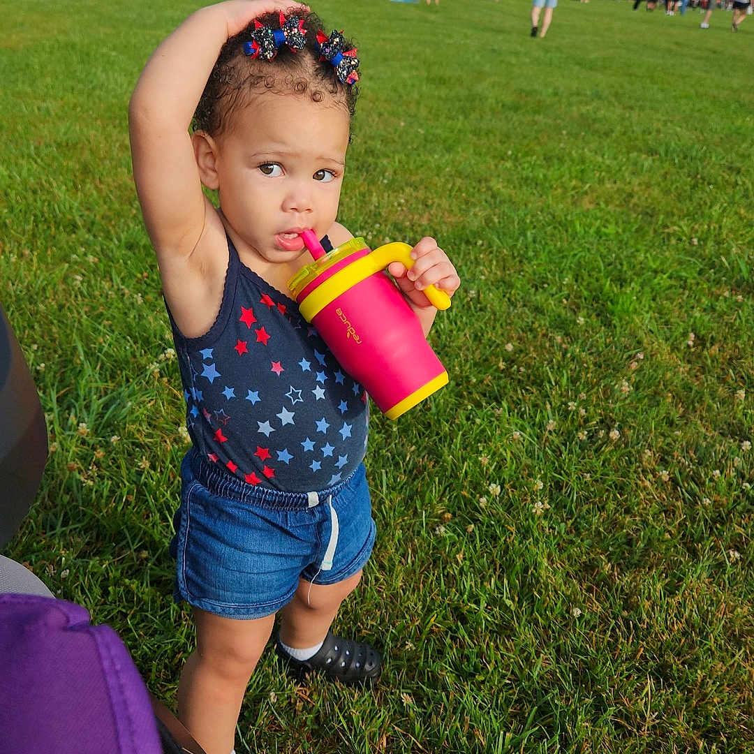 Zafrina is registered to the contest to win money with this photo: baby, bottle, clothing, face, field, grass, grassland, head, lawn, machine, nature, outdoors, park, person, photography, plant, portrait, shaker, shorts, summer