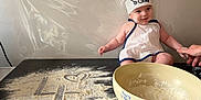 Eden participe au concours pour gagner de l'argent avec cette photo : apron, baby, chef_hat, child, cooking, cute, face, flour, hand, indoor, infant, kitchen, messy, mixing_bowl, person, playful, small, smile, table, white