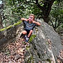 boy, candid, casual_clothing, child, daylight, forest, fun, glasses, leaves, moss, nature, outdoor, playful, rock, shorts, silly_face, smile, sneakers, trees, young
