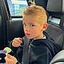 black_hoodie, blue_jeans, boy, car_interior, casual_clothing, child, child_in_car, curious_expression, daylight, hand, indoors, lollipop, looking_at_camera, portrait, seat, seatbelt, seatbelt_on, spiky_hair, window, young