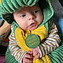 Theo joined the competition — help win amazing prizes! baby, child, costume, dinosaur, green, yellow, hood, cute, hands, face, expression, striped_clothing, indoor, person, infant, soft_texture, playful, curious, holding, tattoo