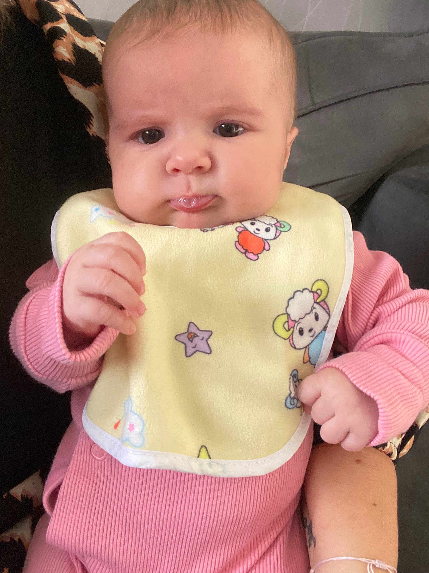 Perle a rejoint le concours — aidez-le/la à gagner de superbes lots ! baby, infant, pink_clothing, bib, drool, hand, person, couch, indoor, patterned_cushion, cute, face, expression, holding, adult_arm, skin, closeup, seated, child, young
