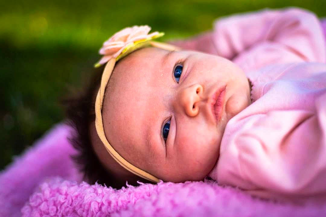 Sarah is registered to the contest to win money with this photo: baby, baby_toddler_clothing, cheek, eye, eyebrow, flash_photography, grass, happy, headband, headgear, headwear, iris, lip, magenta, person, petal, pink, plant, purple, skin