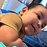 child, toddler, smiling, face, portrait, indoors, bed, bedding, shirt, brown_shirt, lying_down, leaning, close_up, happy, playful, candid, bedroom, home, arm, photography