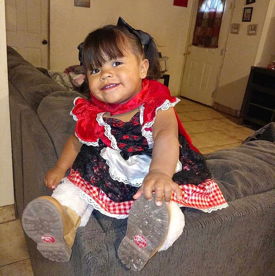 Kehlani joined the competition — help win amazing prizes! toddler, child, smiling, boots, dress, red, black, white, couch, indoor, living_room, happy, girl, floor, hair_bow, portrait, cute, clothing, furniture, playful