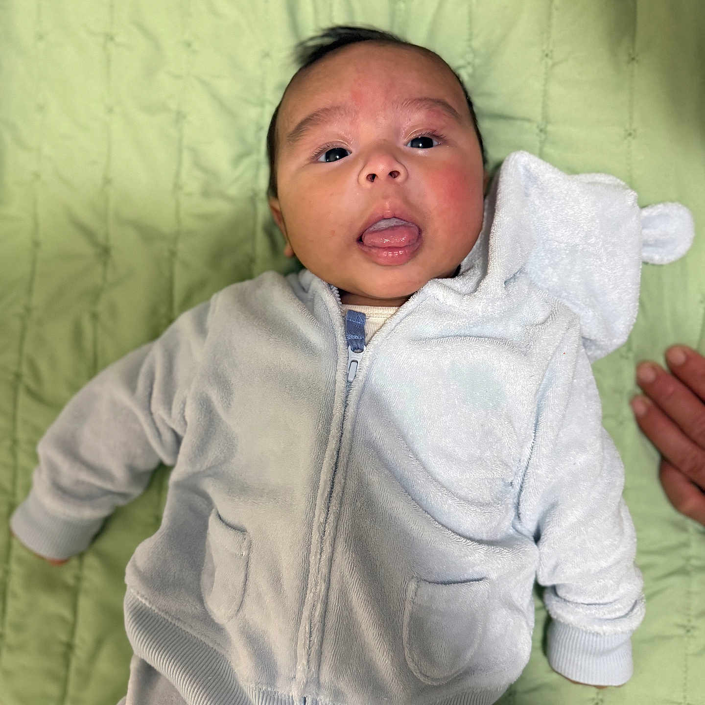Mariano joined the competition — help win amazing prizes! apparel, baby, blanket, child, cute, face, green_blanket, hand, hoodie, indoor, infant, lying_down, person, pocket, portrait, soft_texture, tongue_out, white_clothing, young_child, zipped_jacket