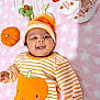 baby, smiling, pumpkin, hat, striped_clothing, baby_shoes, toy, blanket, pink, orange, cute, infant, laying_down, happy, face, child, soft_texture, star_pattern, fall, seasonal