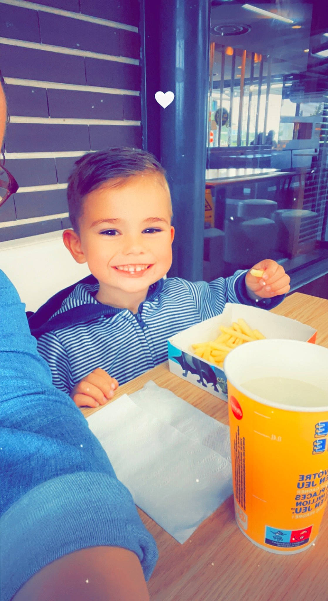 Sacha participe au concours pour gagner de l'argent avec cette photo : baby_toddler_clothing, bookcase, chair, child, comfort_food, cup, drink, drinkware, fun, happy, joy, orange, person, plastic, room, shelf, sitting, smile, t_shirt, table