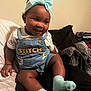 baby, child, smile, headband, bow, socks, denim_overalls, stitch, clothing, indoor, bed, blanket, fabric, happy, cute, person, skin, face, seated, toddler