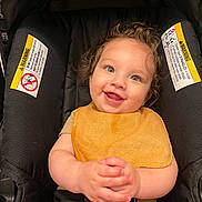 Kyrie joined the competition — help win amazing prizes! baby, child, car_seat, smile, curly_hair, blue_eyes, yellow_bib, happy, infant, seatbelt, clothing, hands, portrait, cute, indoor, person, toddler, sitting, closeup, face