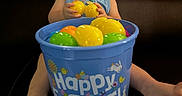 Javan is registered to the contest to win money with this photo: toddler, child, smiling, easter, plastic_eggs, bucket, blue_bucket, yellow_eggs, green_eggs, orange_egg, indoor, leather_couch, happy, sitting, clothing, person, toy, celebration, holiday, festive