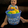 toddler, child, smiling, easter, plastic_eggs, bucket, blue_bucket, yellow_eggs, green_eggs, orange_egg, indoor, leather_couch, happy, sitting, clothing, person, toy, celebration, holiday, festive