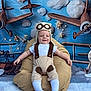 airplanes, aviator_hat, baby, beanbag, blue_background, child, clouds, costume, cute, decor, fun, indoor, infant, playful, portrait, seat, smiling, socks, white_shirt, young