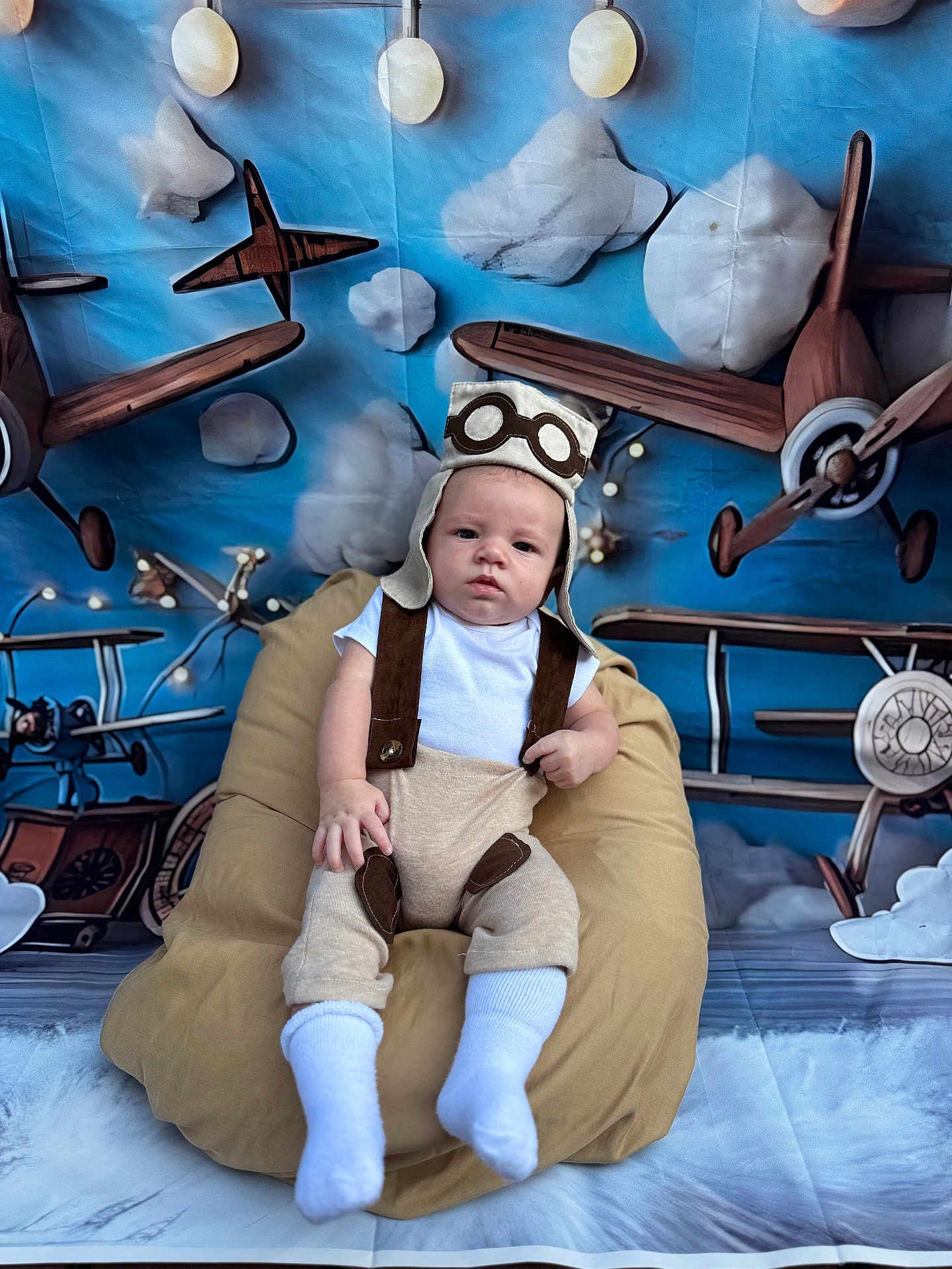 Javan Mccormick joined the competition — help win amazing prizes! airplanes, baby, background, bean_bag, blue_sky, child, clouds, costume, cute, fabric, floor, indoor, infant, photography, pilot_hat, playful, portrait, seated, suspenders, white_socks