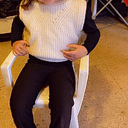 Maelya a rejoint le concours — aidez-le/la à gagner de superbes lots ! child, girl, smiling, pigtails, white_vest, black_shirt, black_pants, sneakers, plastic_chair, indoor, floor, clothing, person, happy, seated, portrait, casual, young_child, home, warm_lighting