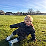 child, toddler, grass, outdoor, smile, blue_sky, jacket, rain_boots, playful, sunny, field, nature, daylight, happy, blond_hair, casual_clothing, park, young, cute, portrait