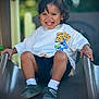 child, toddler, smiling, slide, playground, outdoor, white_tshirt, cartoon_print, shorts, shoes, socks, happy, playing, fun, leisure, summer, daylight, portrait, cute, active