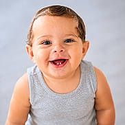Ziad is registered to the contest to win money with this photo: baby, smiling, face, eyes, teeth, skin, child, happy, portrait, sitting, clothing, tank_top, cute, infant, young_child, person, indoors, studio_lighting, head, expression