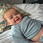 Alfred joined the competition — help win amazing prizes! baby, smiling, face, infant, blue_sweater, pillow, bed, blanket, indoor, child, happy, cute, skin, head, person, young, cozy, comfort, lying_down, portrait