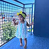 Alaïa joined the competition — help win amazing prizes! toddler, child, yellow_bow, striped_dress, barefoot, balcony, blue_floor, metal_fence, outdoor, sunny_day, mountains, parking_lot, playful, happy, standing, curly_hair, daylight, person, smiling, railing