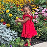 Alaïa joined the competition — help win amazing prizes! toddler, child, red_dress, flowers, garden, plants, greenery, outdoor, nature, smiling, curious, side_view, portrait, colorful, footpath, young_child, sunlight, summer, happy, braided_hair