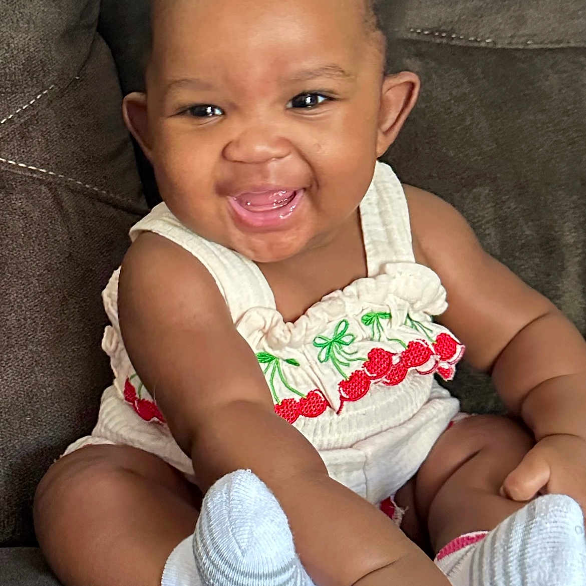 Jahzara joined the competition — help win amazing prizes! baby, cherry_pattern, child, couch, cute, cute_outfit, dark_background, face, hand, happy, indoors, infant, person, portrait, sitting, smiling, socks, toddler, white_clothing, young_child